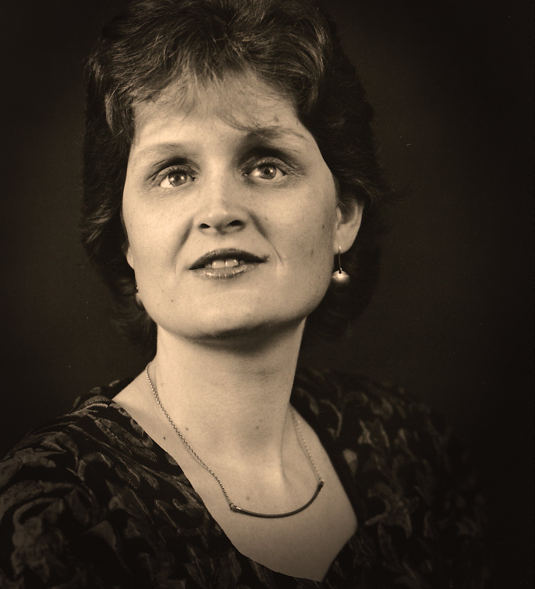 Portrait photograph of Lisette Wesseling wearing a dark patterned dress and necklace, looking directly at the camera with a warm expression